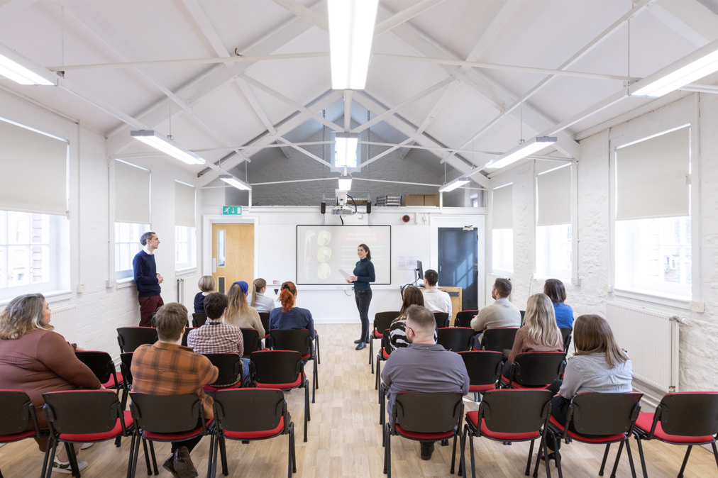 an audience sitting in rows listening to a speaker in a large white room